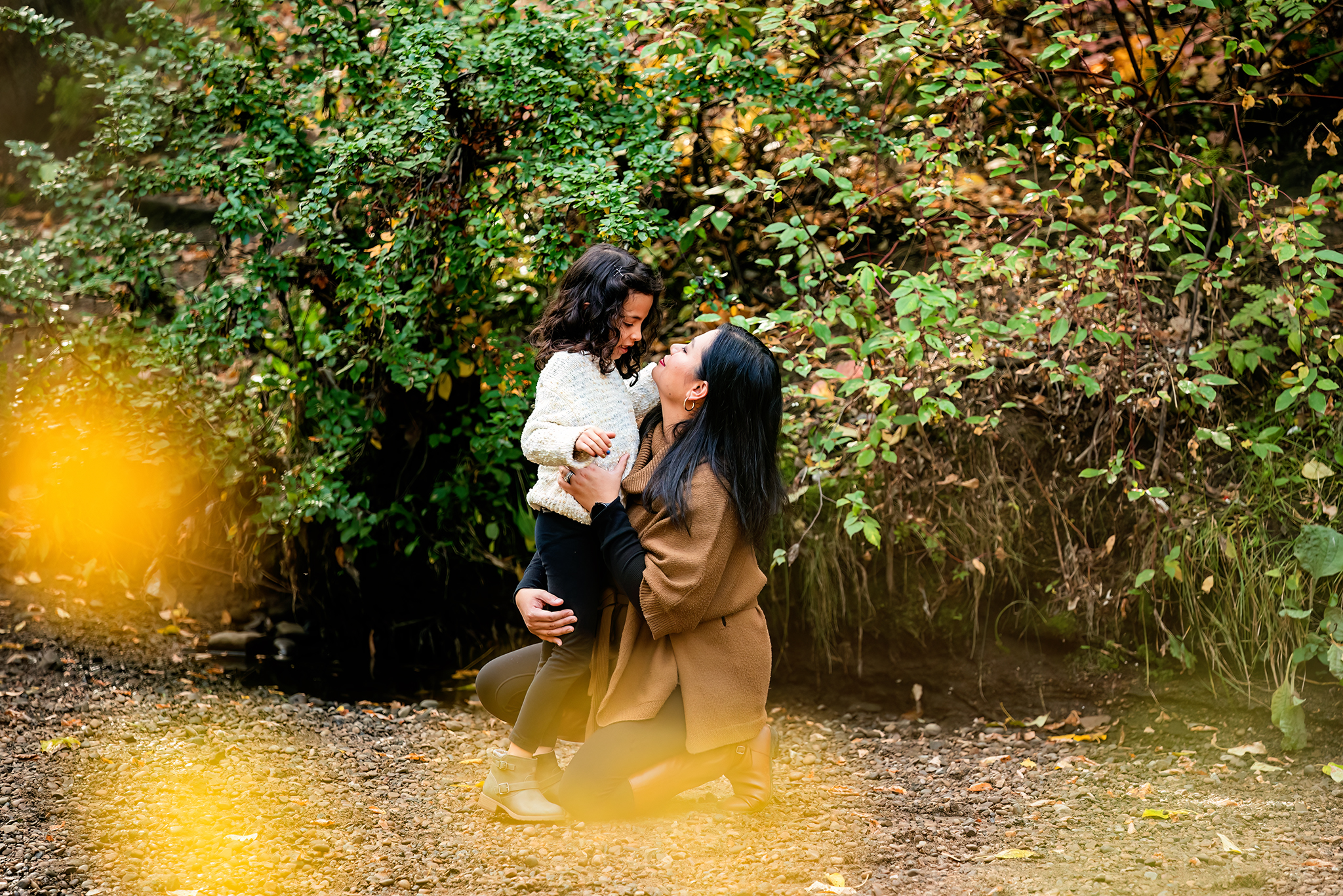 mom and daughter stand near trees along ravine bank yellow bokeh framing outdoor family photography session edmonton ravine