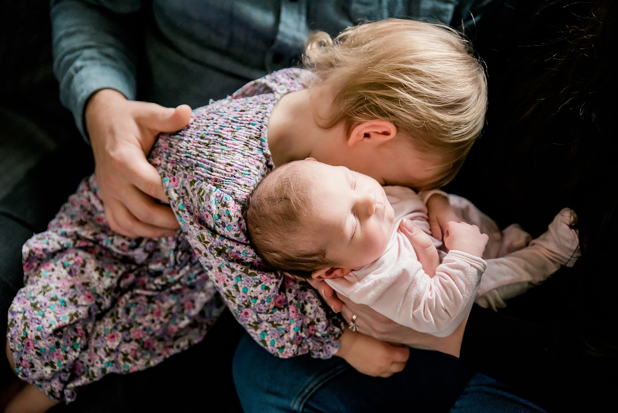 parents hands hold daughters toddler hugs baby holding her tiny hand in home lifestyle newborn photoshoot strathcona county alberta