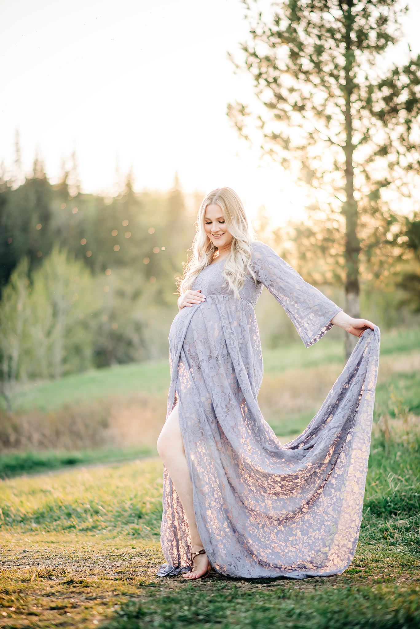 expectant mother embraces baby bump holds lace dress backlit golden hour maternity photography session edmonton alberta
