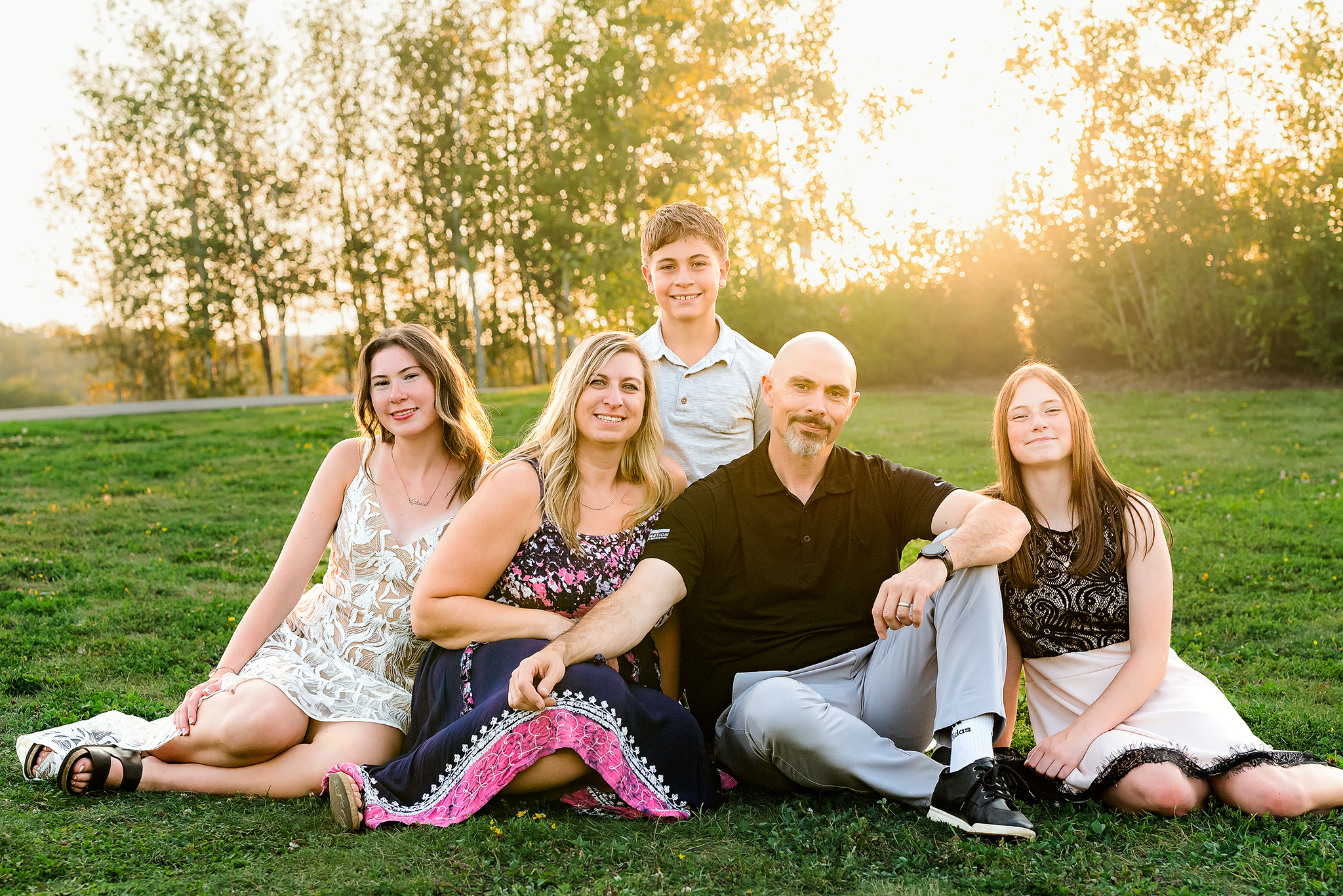 family of five sitting on grassy hill golden hour sun flare cascading behind them family photographer edmonton