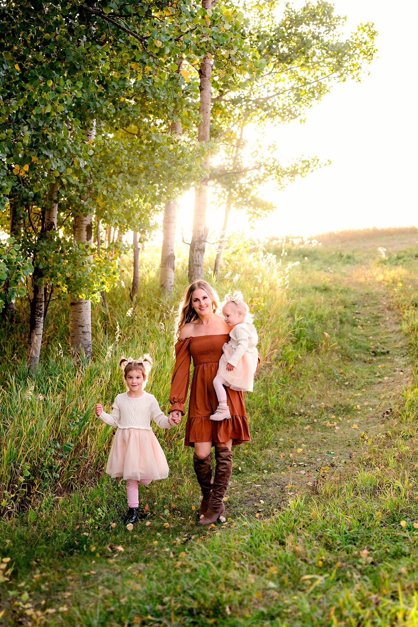 mom two daughters walking on treed path autumn colors golden hour sunflare over hill outdoor motherhood photography session lacombe county alberta