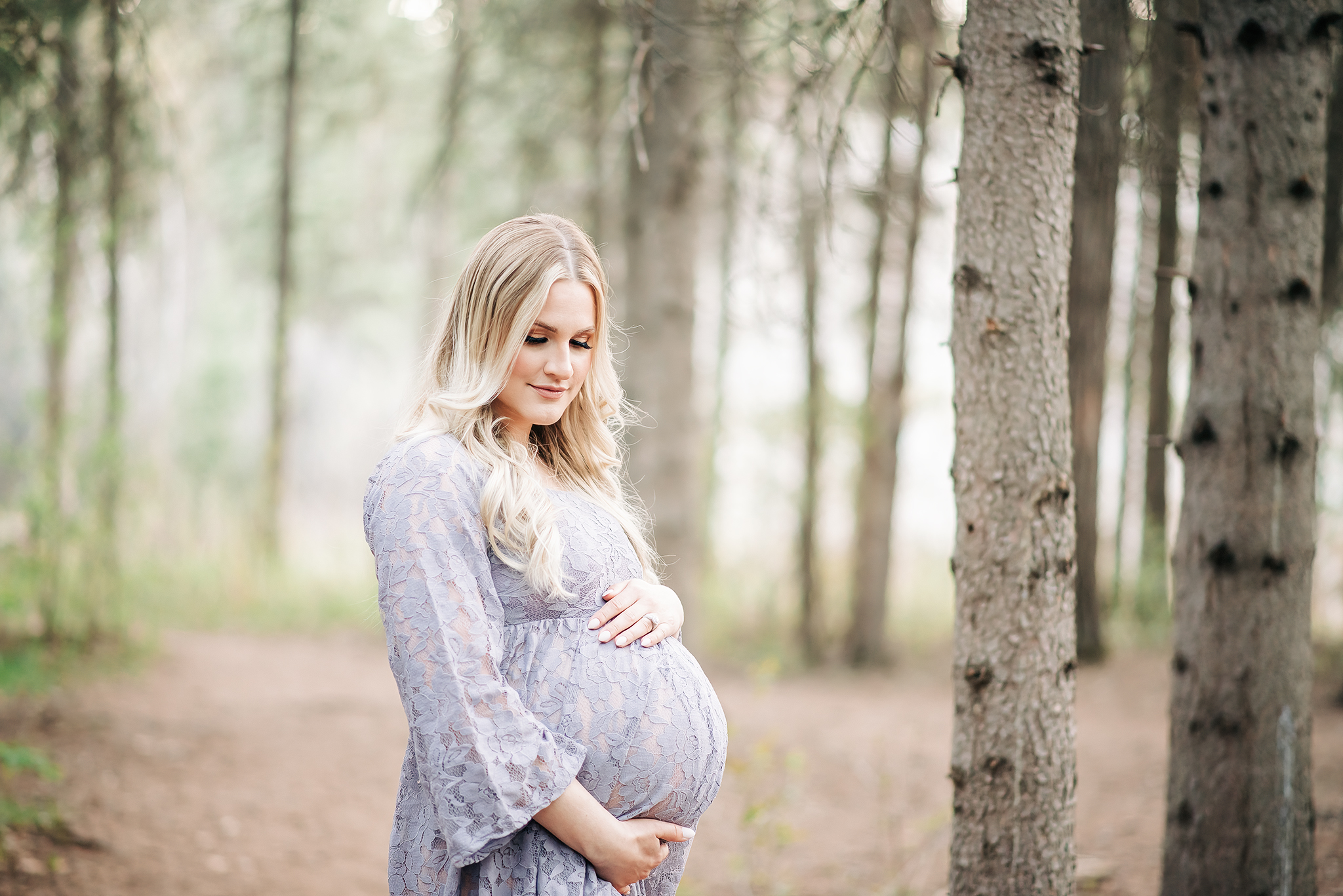 pregnant woman holds belly while looking down standing in a forest edmonton maternity session