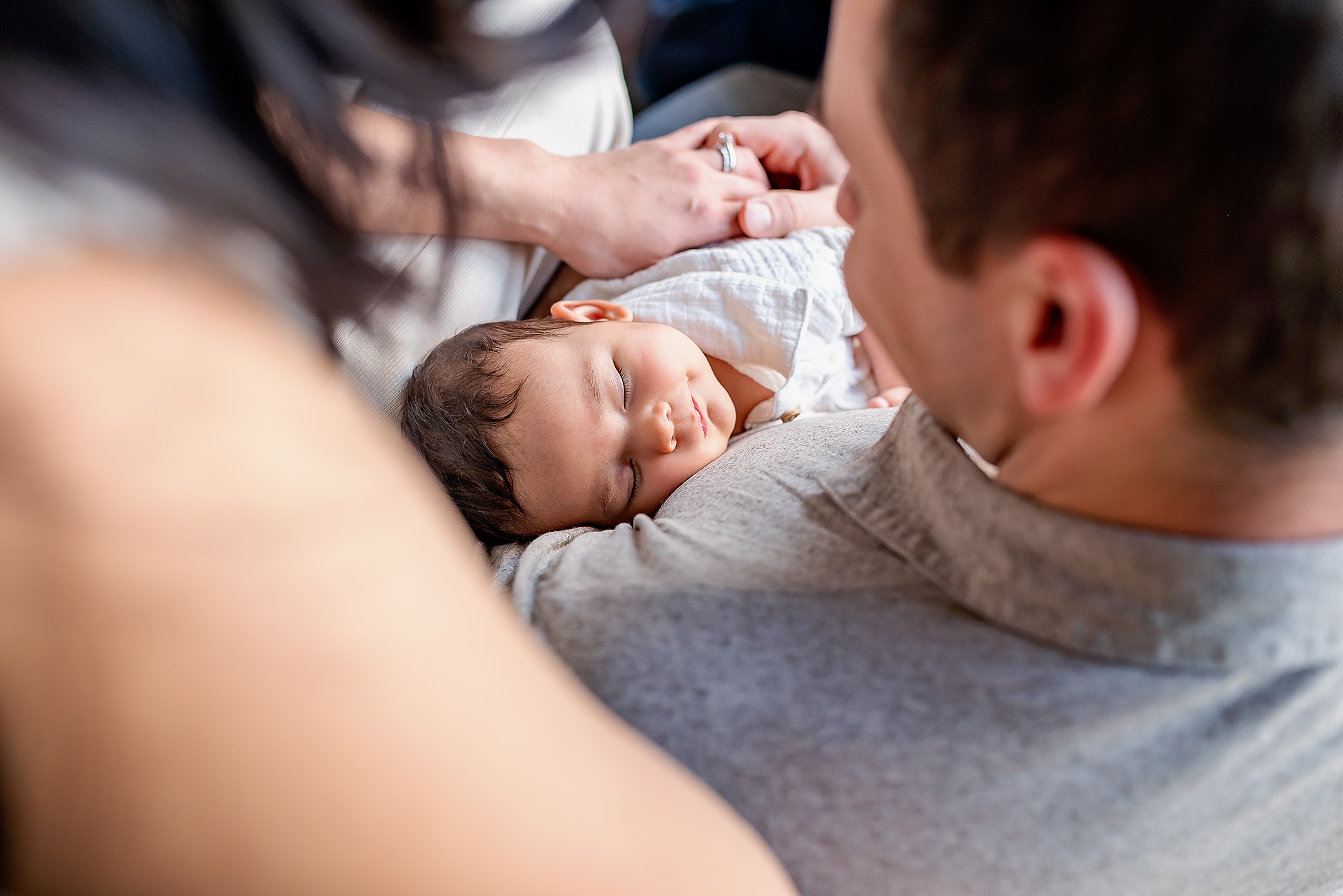 baby girl smiles nestled between parents photo over mom and dads shoulders lifestyle newborn photography session sherwood park ab