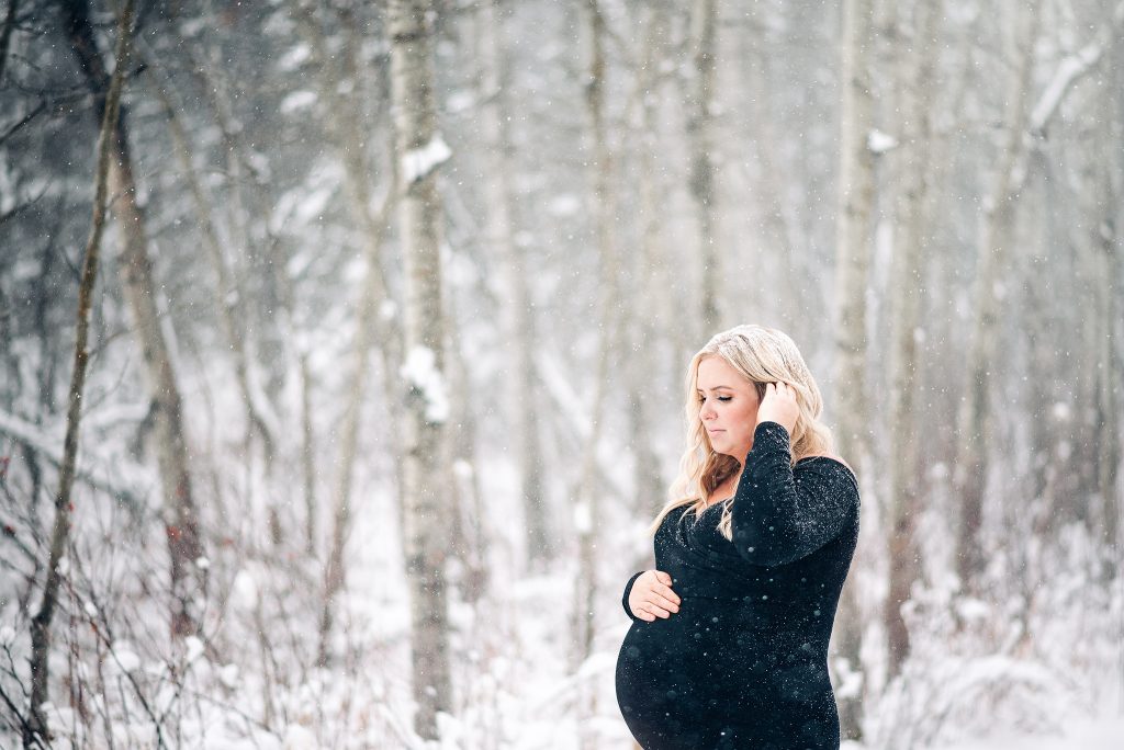 Expecting mama holding pregnant belly smiling snowing winter maternity photo session sherwood park Alberta