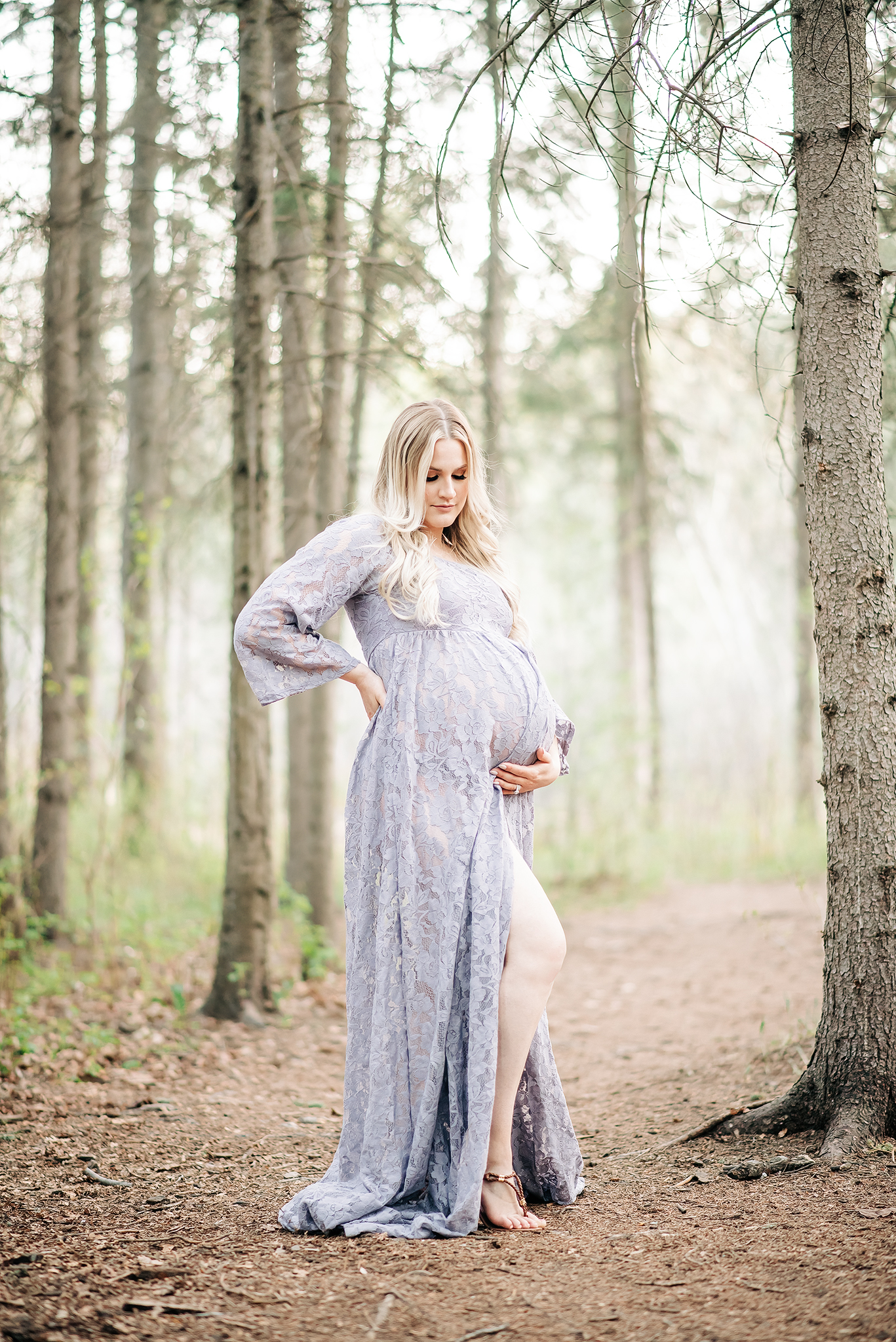 pregnant woman holds belly while looking down standing in a forest edmonton maternity session