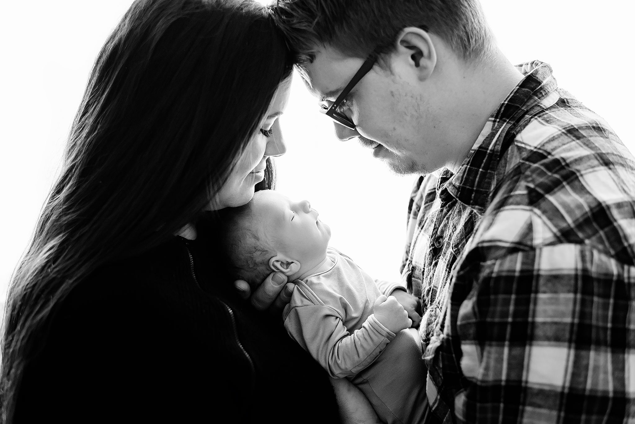 mom and dad white background hold baby between them in home newborn photos fort sask