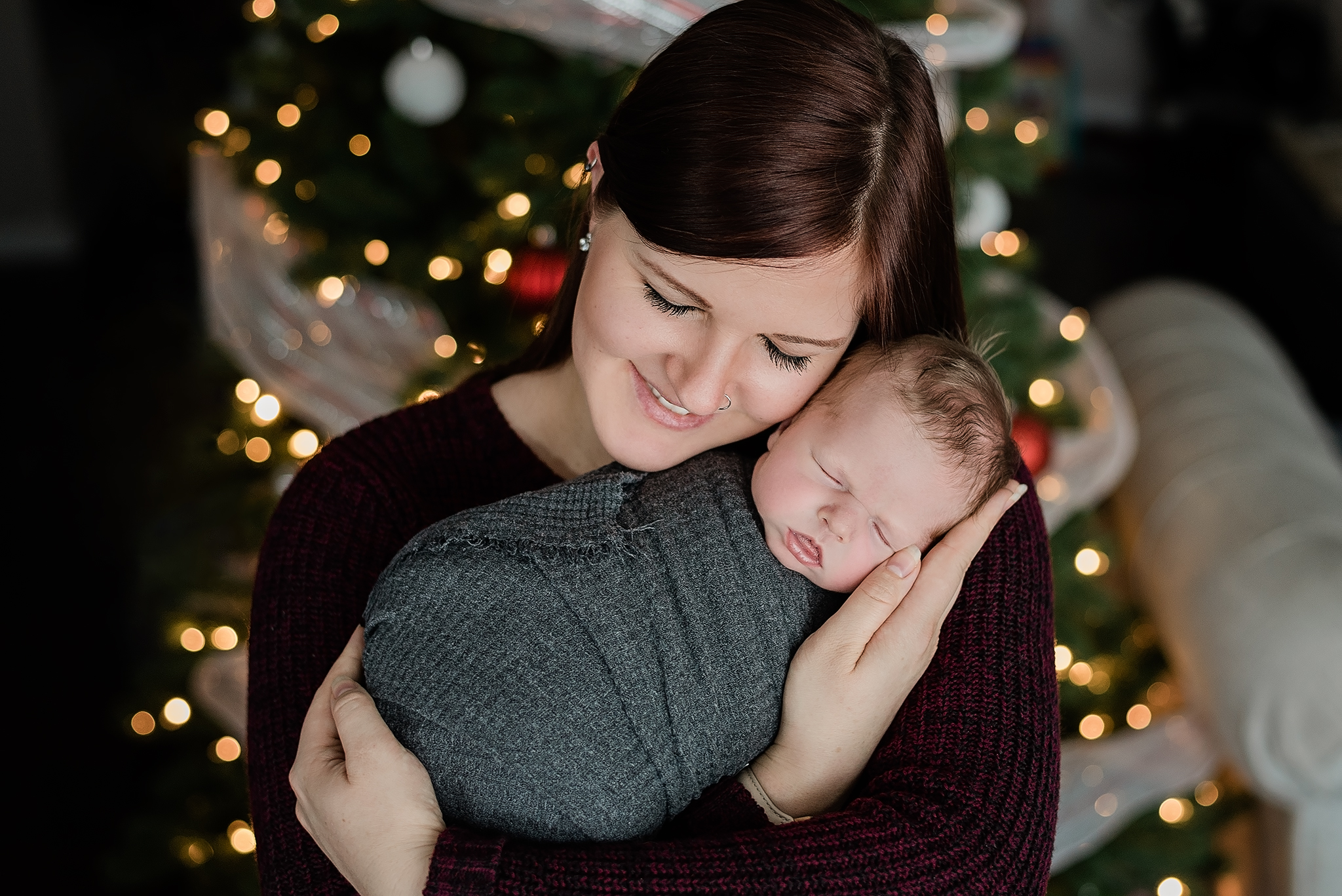 mom holds baby boy christmas tree lights in background yeg newborn photography