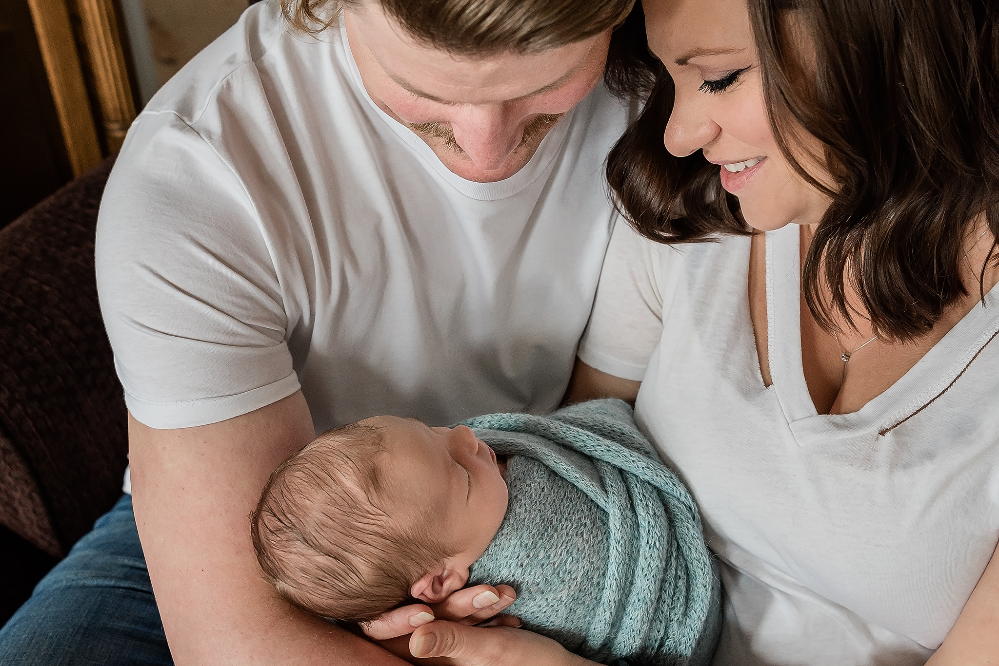parents sit close admiring newborn baby during in home newborn photoshoot sherwood park