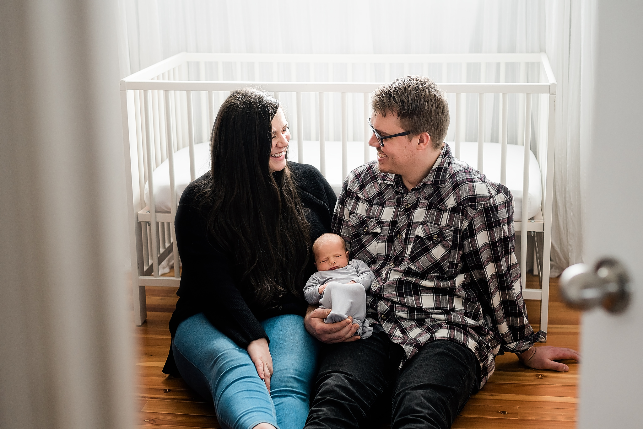 parents smile at eachother sitting in front of baby crib in home newborn photos edmonton ab
